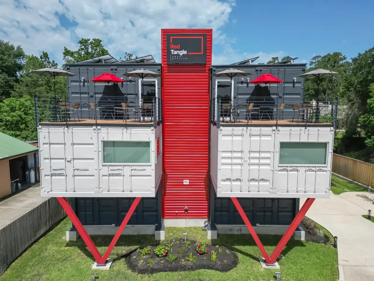 Red Tangle Workspaces exterior: stacked charcoal and white shipping containers on red steel columns in Magnolia, TX